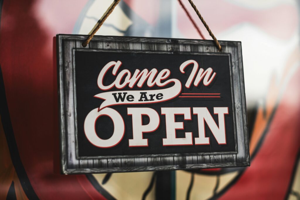 A close-up of a welcoming 'We Are Open' sign at a café entrance in Paso Robles, CA.